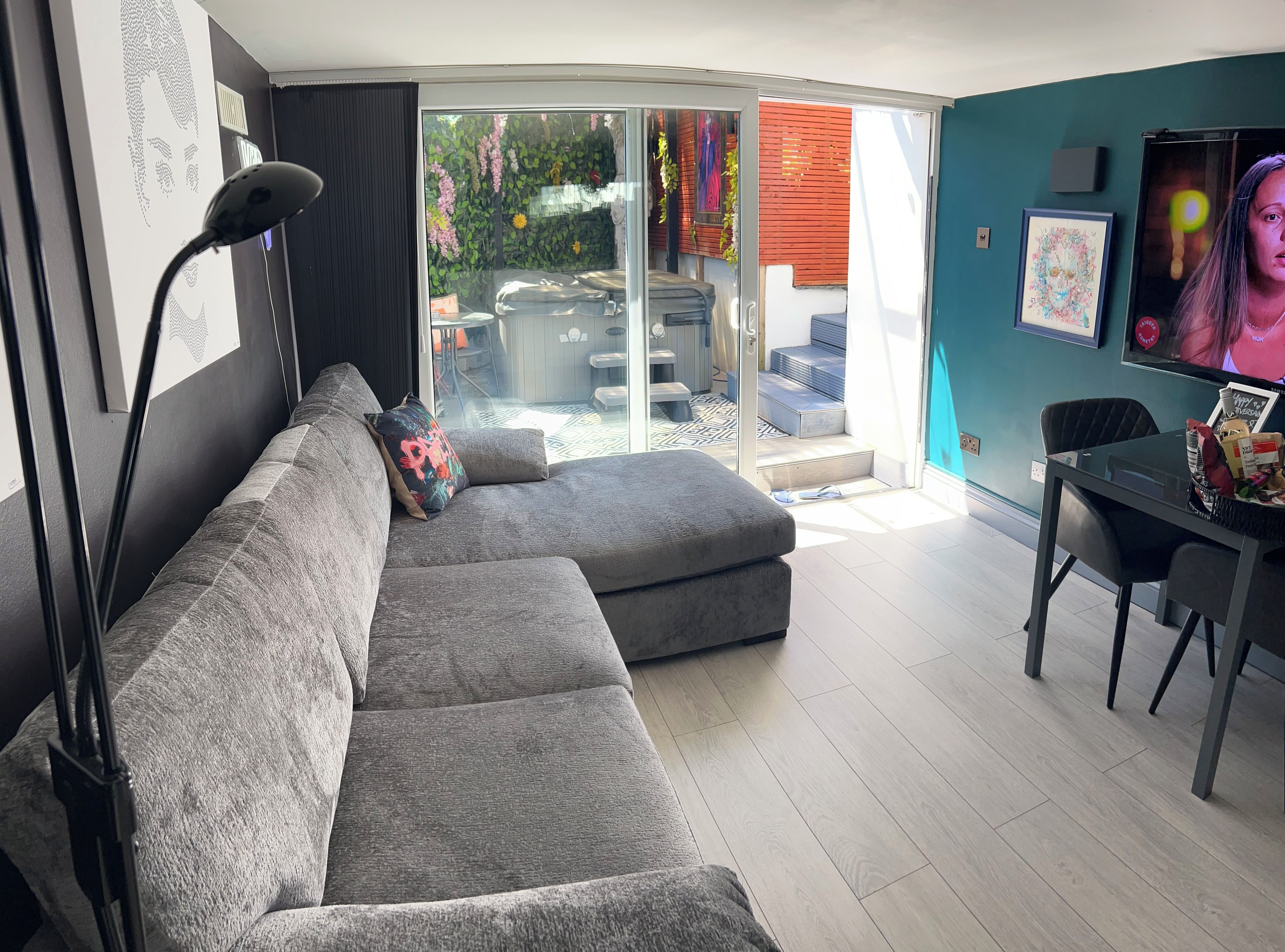 A modern living room with a grey sectional sofa, a dining table with chairs, and a large sliding glass door leading to an outdoor area.