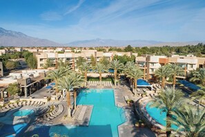 A resort with multiple swimming pools, palm trees, and a mountainous backdrop.