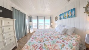 A bedroom with a large bed, a dresser, a painting of sailboats, and a view of the sea through the window. - Oceanfront, Central, Huge 5k sq ft Home w Huge Private Pool, Hot tub, & Gameroom (North Myrtle Beach)