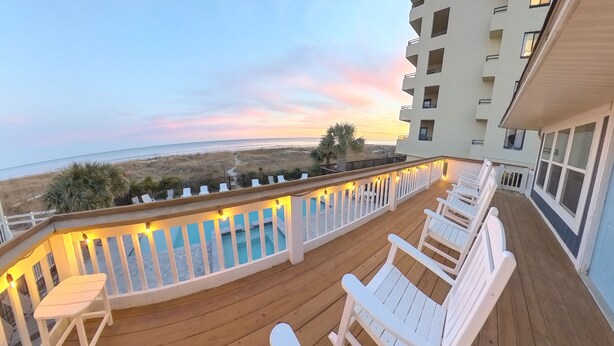 A balcony with white chairs and a pool, overlooking a beach and ocean during sunset. - Oceanfront, Central, Huge 5k sq ft Home w Huge Private Pool, Hot tub, & Gameroom (North Myrtle Beach)