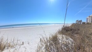 A beach with a clear sky, sandy shore, and buildings in the background. - Oceanfront, Central, Huge 5k sq ft Home w Huge Private Pool, Hot tub, & Gameroom (North Myrtle Beach)