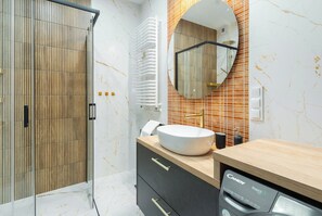 Features a large, round sink, washing machine, and a stylish mirror above.