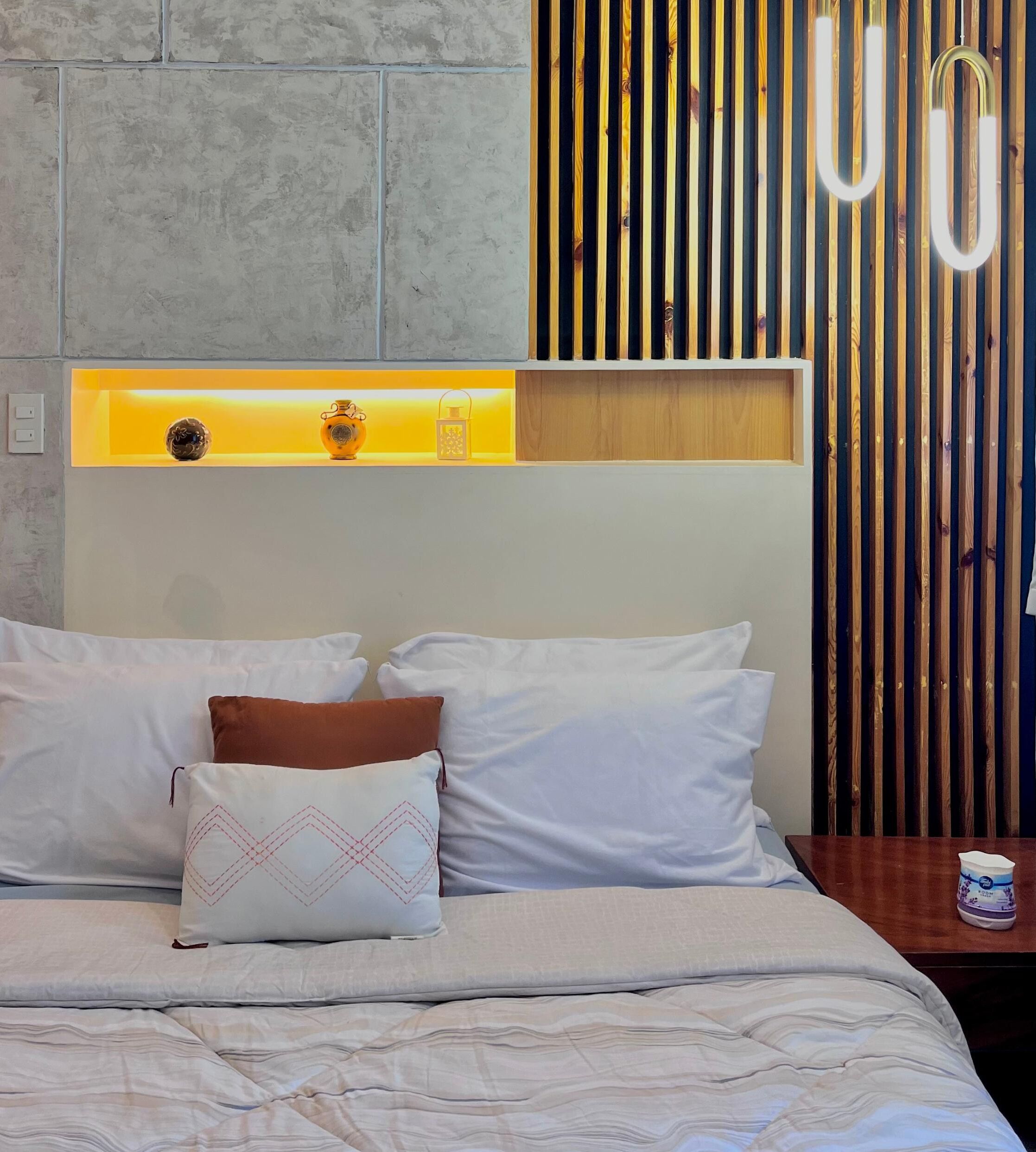 A bedroom with a bed, pillows, a nightstand, a lamp, and a wooden slat wall.