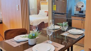 A modern kitchen with a refrigerator, microwave, and dining area with a glass table set for two. - Room-simple, Modern & Cozy Condo in Lafa (Iloilo)