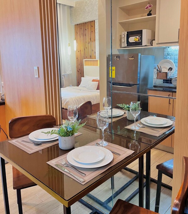 A modern kitchen with a refrigerator, microwave, and dining area with a glass table set for two. - Room-simple, Modern & Cozy Condo in Lafa (Iloilo)