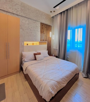 A modern bedroom with a large bed, wooden headboard, and a view of the outdoors through a window.
