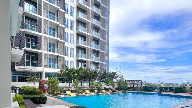 A residential building with a swimming pool, a balcony with a railing, and a view of the surrounding area. - Room-simple, Modern & Cozy Condo in Lafa (Iloilo)