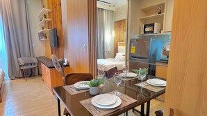 A modern dining area with a wooden table set for two, a sofa, and a TV mounted on the wall. - Room-simple, Modern & Cozy Condo in Lafa (Iloilo)