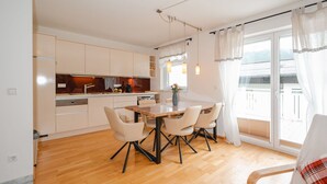 A modern kitchen with a dining area, wooden flooring, and a view of the outdoors through large windows. - Lovely apartment for 3 guests with TV and terrace (Bad Hofgastein)
