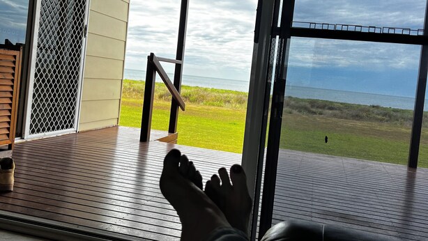Vista desde una habitación con un amplio ventanal que da a una zona verde y una masa de agua.