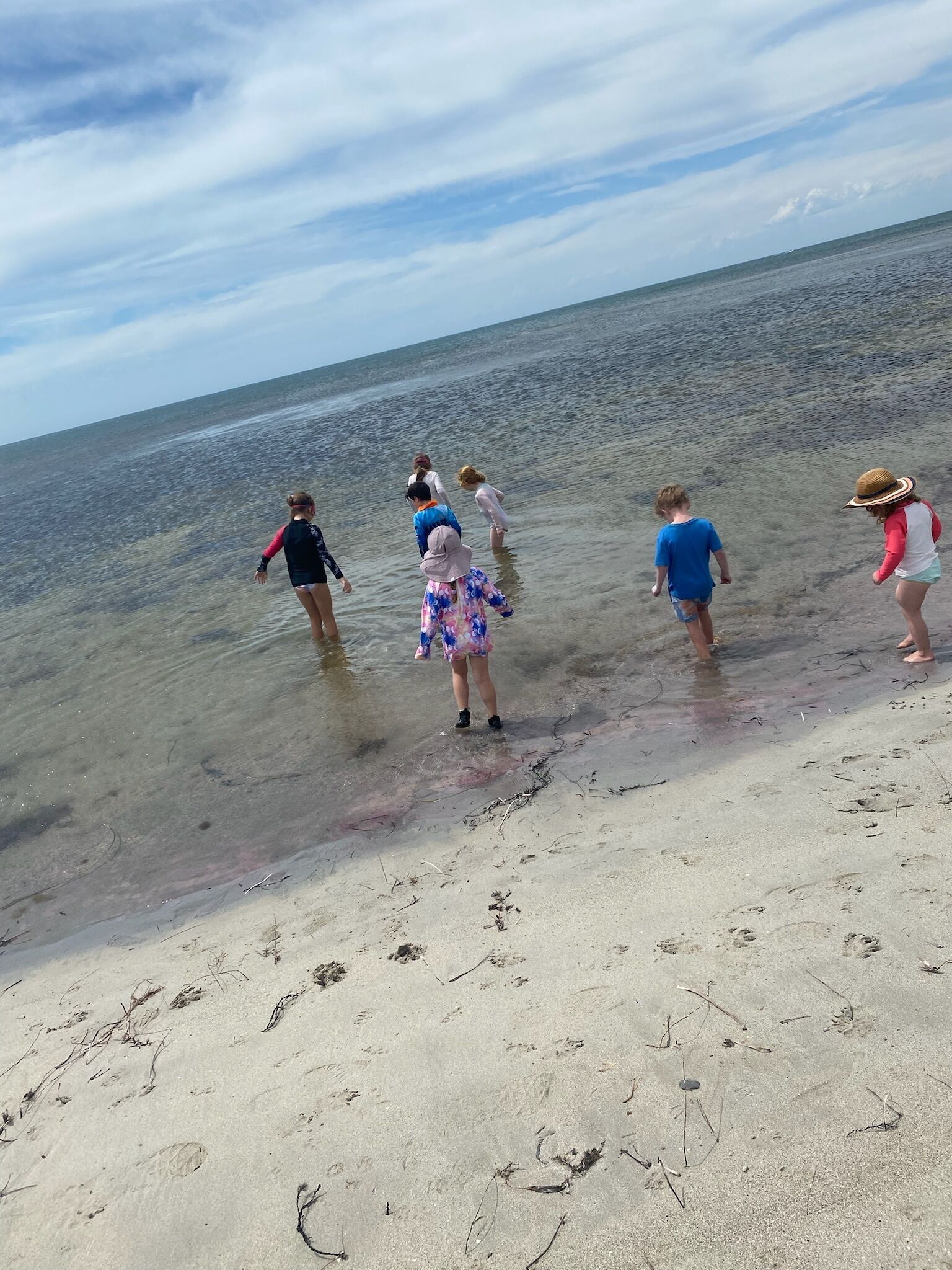 Una playa con agua cristalina y poca profundidad, y huellas en la arena.