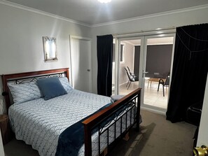 Une chambre à coucher comprenant un lit, une table de chevet, une fenêtre avec des rideaux et une porte donnant sur un balcon.