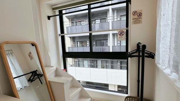 A room with a large window, a mirror, a black metal rack, and a wooden floor.