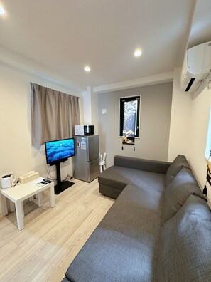 Una sala de estar moderna con un sofá gris, un televisor de pantalla plana, un microondas y un refrigerador.