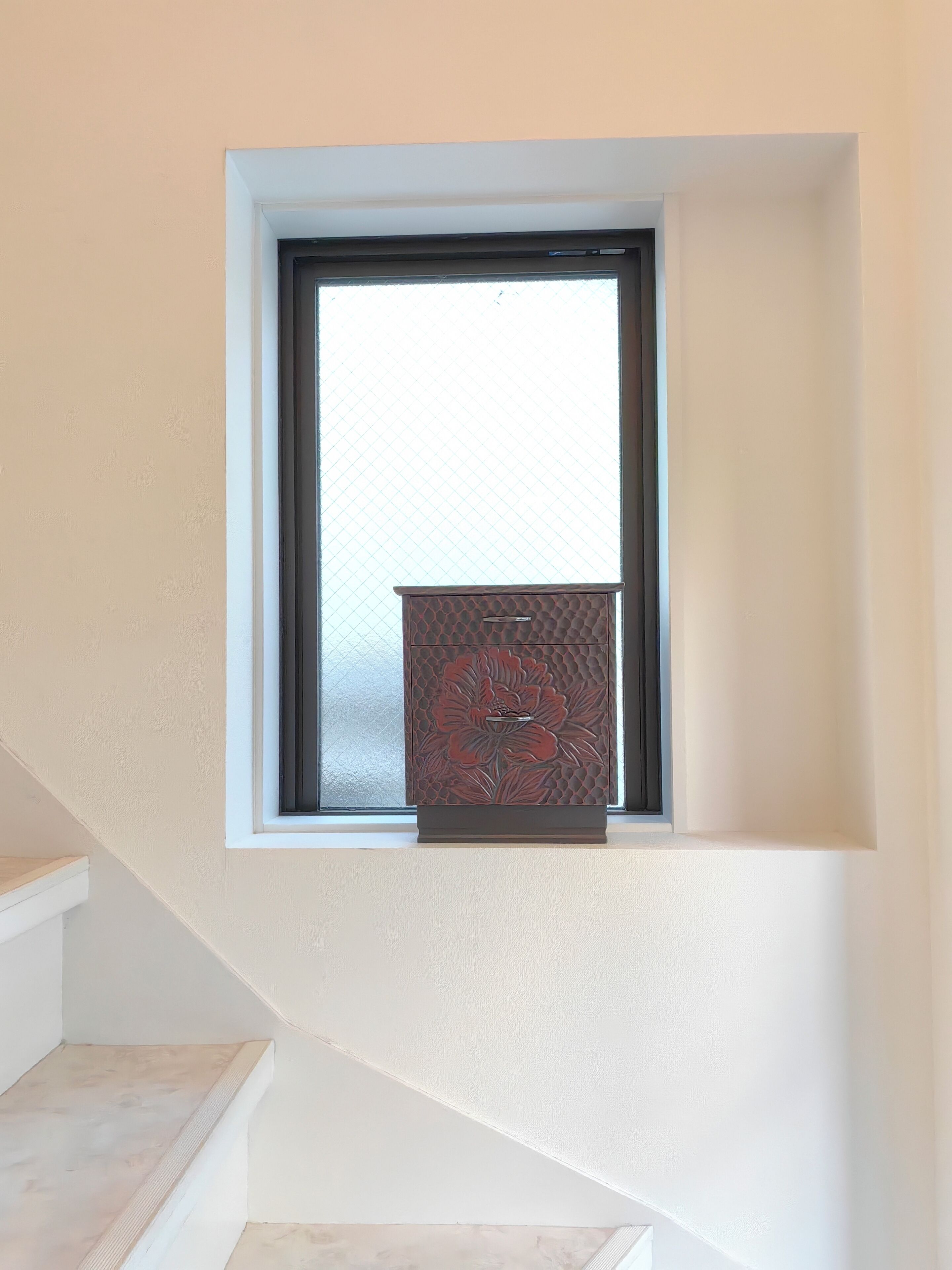 A small window with a decorative cabinet below it.