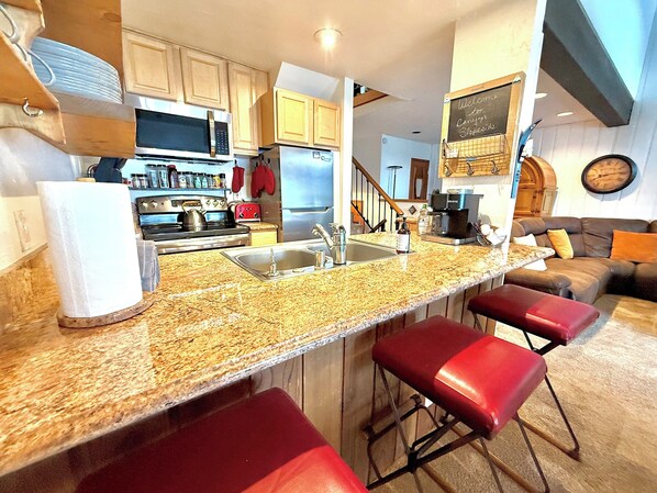 A kitchen with a granite countertop, stainless steel appliances, and a red bar stool. - Slopeside Retreat at Mammoth Mountain, Ski-in\Ski-out at Canyon Lodge (Mammoth Lakes)