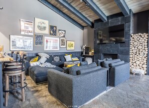 A modern living room with a grey sofa set, a flat-screen TV mounted on the wall, and a fireplace with a log stack. - Slopeside Retreat at Mammoth Mountain, Ski-in\Ski-out at Canyon Lodge (Mammoth Lakes)