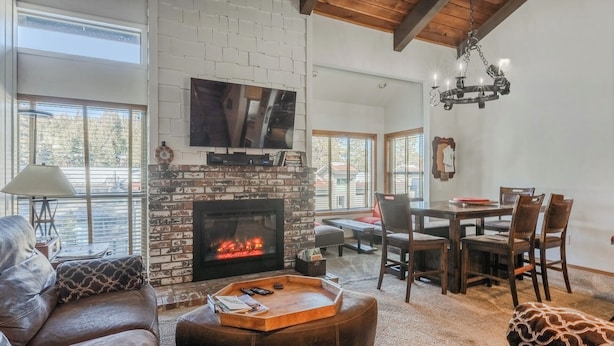 A living room with a fireplace, a television mounted on the wall, a dining area with a table and chairs, and a sofa with a patterned cushion. - Slopeside Retreat at Mammoth Mountain, Ski-in\Ski-out at Canyon Lodge (Mammoth Lakes)