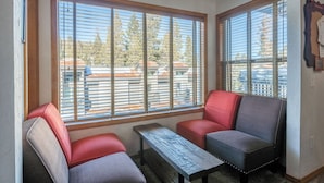 A corner seating area with two chairs and a small table, large windows with blinds, and a view of buildings outside. - Slopeside Retreat at Mammoth Mountain, Ski-in\Ski-out at Canyon Lodge (Mammoth Lakes)