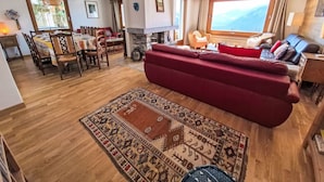 A living room with a red sofa, a patterned rug, a dining area with wooden furniture, and a large window with a mountain view. - Wonderful private villa for 10 guests with WIFI, TV, terrace and panoramic view (Bluche)