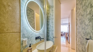 A bathroom with a large oval sink, a mirror, and a frosted glass door leading to a dining area. - Elegant Condo SohoPV Ocean Views & Rooftop Pool Short Description (Puerto Vallarta)