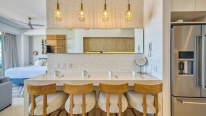 A modern kitchen with a central island, wooden chairs, hanging pendant lights, and a stainless steel refrigerator. - Elegant Condo SohoPV Ocean Views & Rooftop Pool Short Description (Puerto Vallarta)