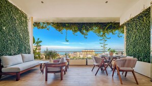 A modern outdoor seating area with a view of the sea, featuring a sofa, chairs, and a table. - Elegant Condo SohoPV Ocean Views & Rooftop Pool Short Description (Puerto Vallarta)