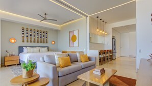 A modern hotel room with a bed, sofa, dining table, and chairs. There is a ceiling fan, wall-mounted lights, and a large mirror. - Elegant Condo SohoPV Ocean Views & Rooftop Pool Short Description (Puerto Vallarta)