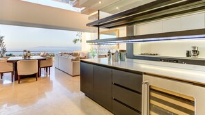 Une cuisine moderne dotée d’un grand îlot central, d’appareils électroménagers intégrés et offrant une vue sur l’océan.