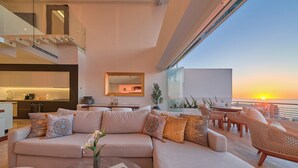 Un salon moderne avec un canapé, une table basse et une vue sur le coucher de soleil sur l’océan.