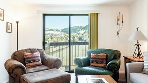 Ein Wohnzimmer mit zwei Ledersesseln, einem Couchtisch und Blick auf eine Stadtlandschaft durch ein großes Fenster.