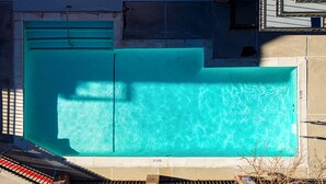 Ein Dachpool mit glasklarer blauer Wasseroberfläche, umgeben von einer gefliesten Liegefläche und einem Metallgeländer.