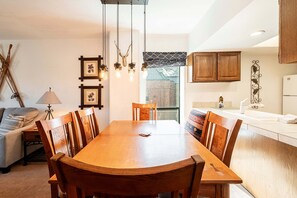 Un comedor con mesa y sillas de madera, una lámpara, cuadros enmarcados en la pared y armarios de madera.