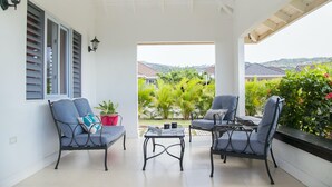 Une terrasse couverte avec deux chaises et une table, une vue sur le jardin et un plafond blanc agrémenté d’un ventilateur.