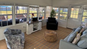 A sunlit room with a view of the backyard, a ceiling fan, a white console table, a black armchair, a wicker ottoman, and a grey sofa with patterned cushions. - Nice House in Perdido Bay (Lillian)