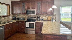 A kitchen with wooden cabinets, granite countertops, stainless steel appliances, and a window with blinds. - Nice House in Perdido Bay (Lillian)