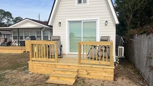 A wooden deck with a railing, a sliding glass door, and a small outdoor seating area with chairs. - Nice House in Perdido Bay (Lillian)