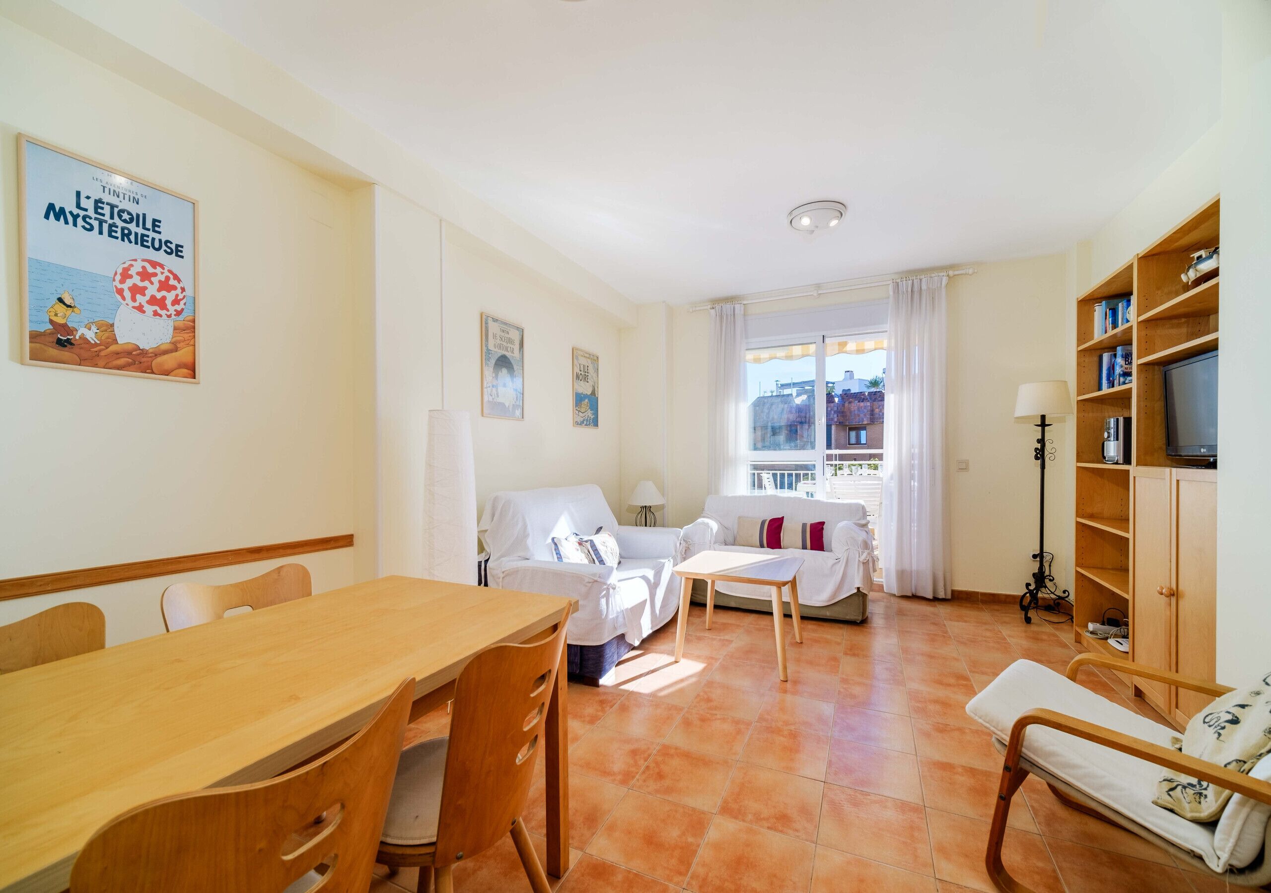 Une pièce comprenant une table à manger en bois, deux canapés blancs, un meuble en bois et un téléviseur.