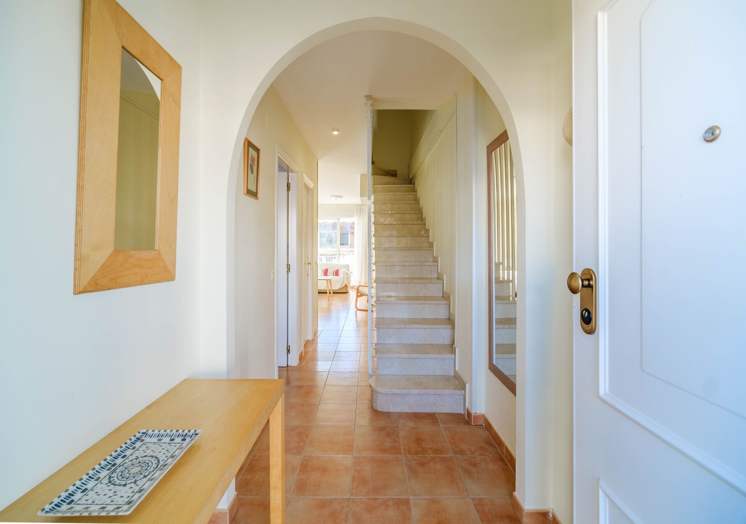 A hallway with a wooden bench, a staircase, and a door with a brass handle.