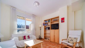 Een woonkamer met een bank, een stoel, een tafel, een boekenkast en een televisie.
