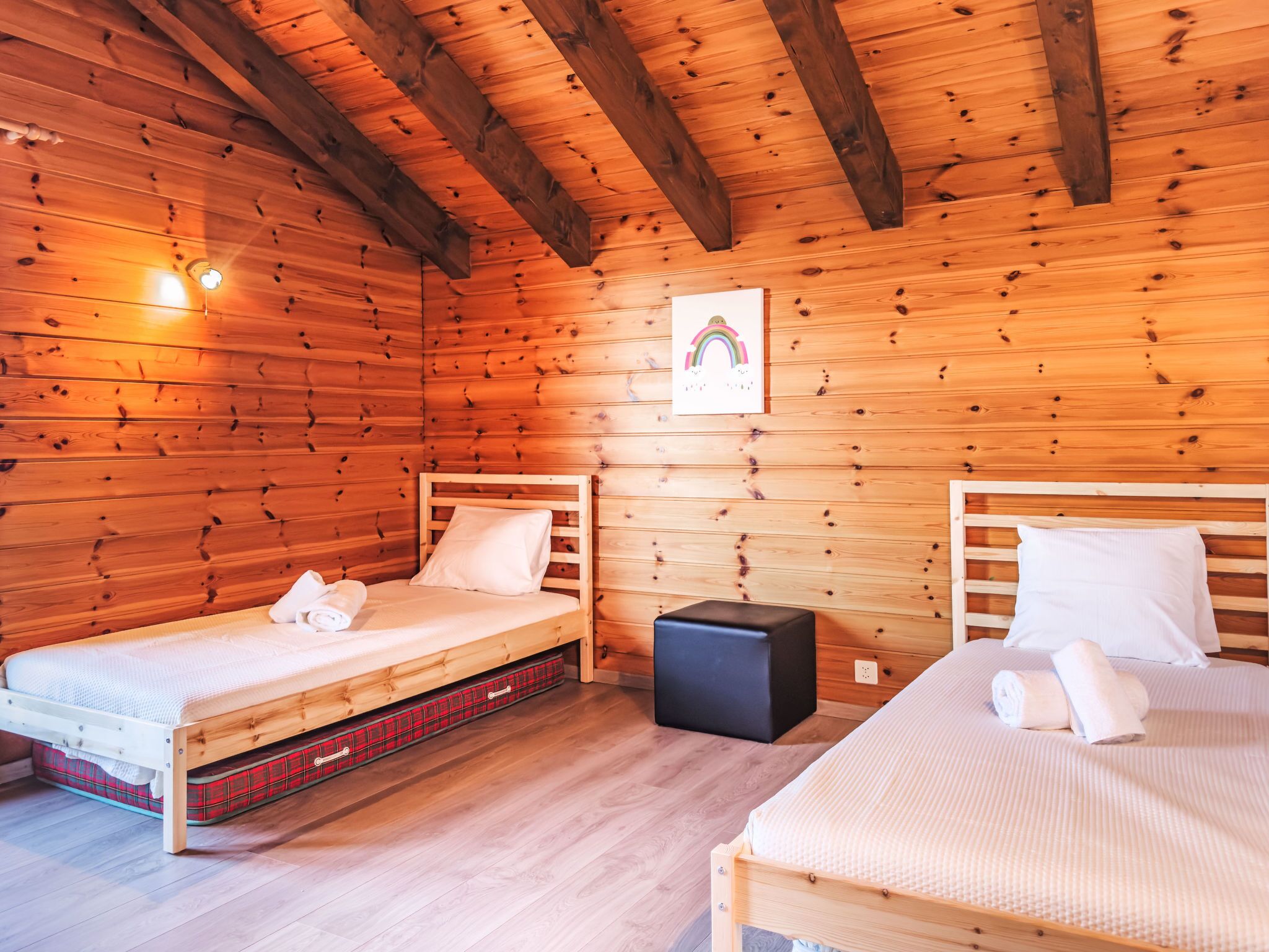 Um quarto de cabana acolhedor com duas camas de madeira, um pequeno banquinho preto e um quadro na parede.