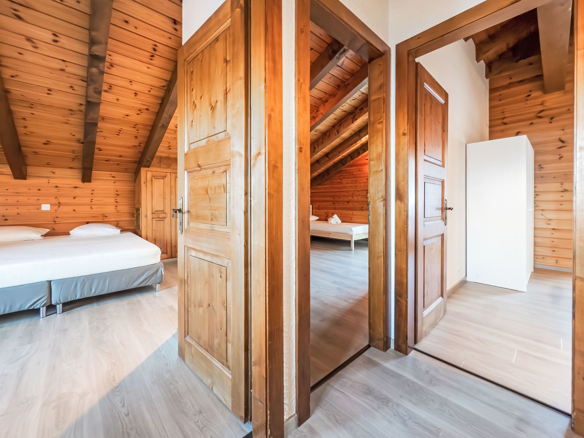 A wooden interior with two bedrooms, each with a bed and a door.