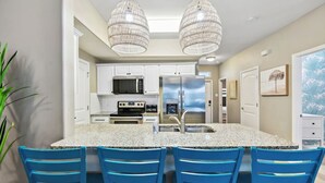 A modern kitchen with white cabinets, stainless steel appliances, and a granite countertop. There are four blue chairs around the table. - Resort Pool, 5 Bedroom, Dog-Friendly, King Bed, Near White Cap Beach, Patio, Grill (Corpus Christi)