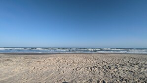 A wide sandy beach with waves approaching the shore under a clear sky. - Resort Pool, 5 Bedroom, Dog-Friendly, King Bed, Near White Cap Beach, Patio, Grill (Corpus Christi)