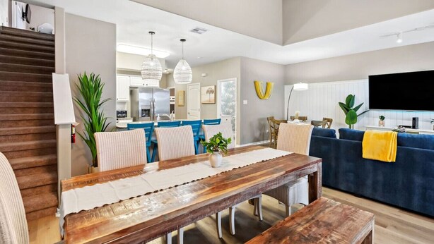 A modern living room with a wooden dining table, blue sofas, and a large flat-screen TV. - Resort Pool, 5 Bedroom, Dog-Friendly, King Bed, Near White Cap Beach, Patio, Grill (Corpus Christi)