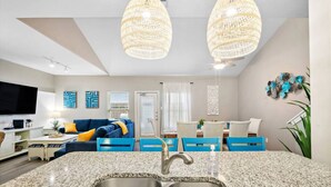 A modern kitchen with granite countertops, stainless steel sink, and a dining area with blue chairs. - Resort Pool, 5 Bedroom, Dog-Friendly, King Bed, Near White Cap Beach, Patio, Grill (Corpus Christi)