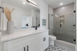 Une salle de bain moderne avec un meuble-lavabo blanc, un grand miroir, des toilettes et une douche séparée par une paroi en verre.