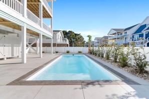 Une piscine dotée d’une terrasse blanche, entourée d’une clôture blanche et de petites plantes.