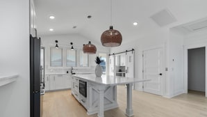 A modern kitchen with white cabinetry, a central island, and pendant lighting. - "Sea Ya at Holden" BRAND NEW 4 Bedroom, 4.5 Bath Home w/ PRIVATE POOL and Elevator! (Holden Beach)