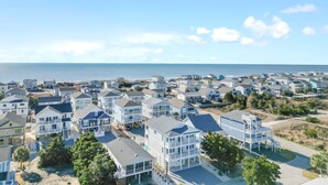 A coastal residential area with multiple two-story houses, a clear view of the ocean, and a sandy beach in the background. - "Sea Ya at Holden" BRAND NEW 4 Bedroom, 4.5 Bath Home w/ PRIVATE POOL and Elevator! (Holden Beach)